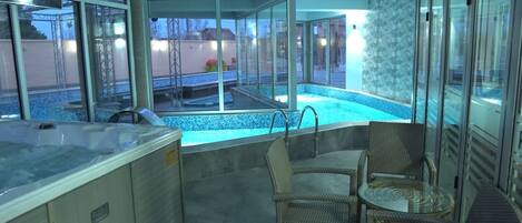Un área de spa con un jacuzzi, dos sillones de mimbre y una piscina con cerramiento de vidrio.