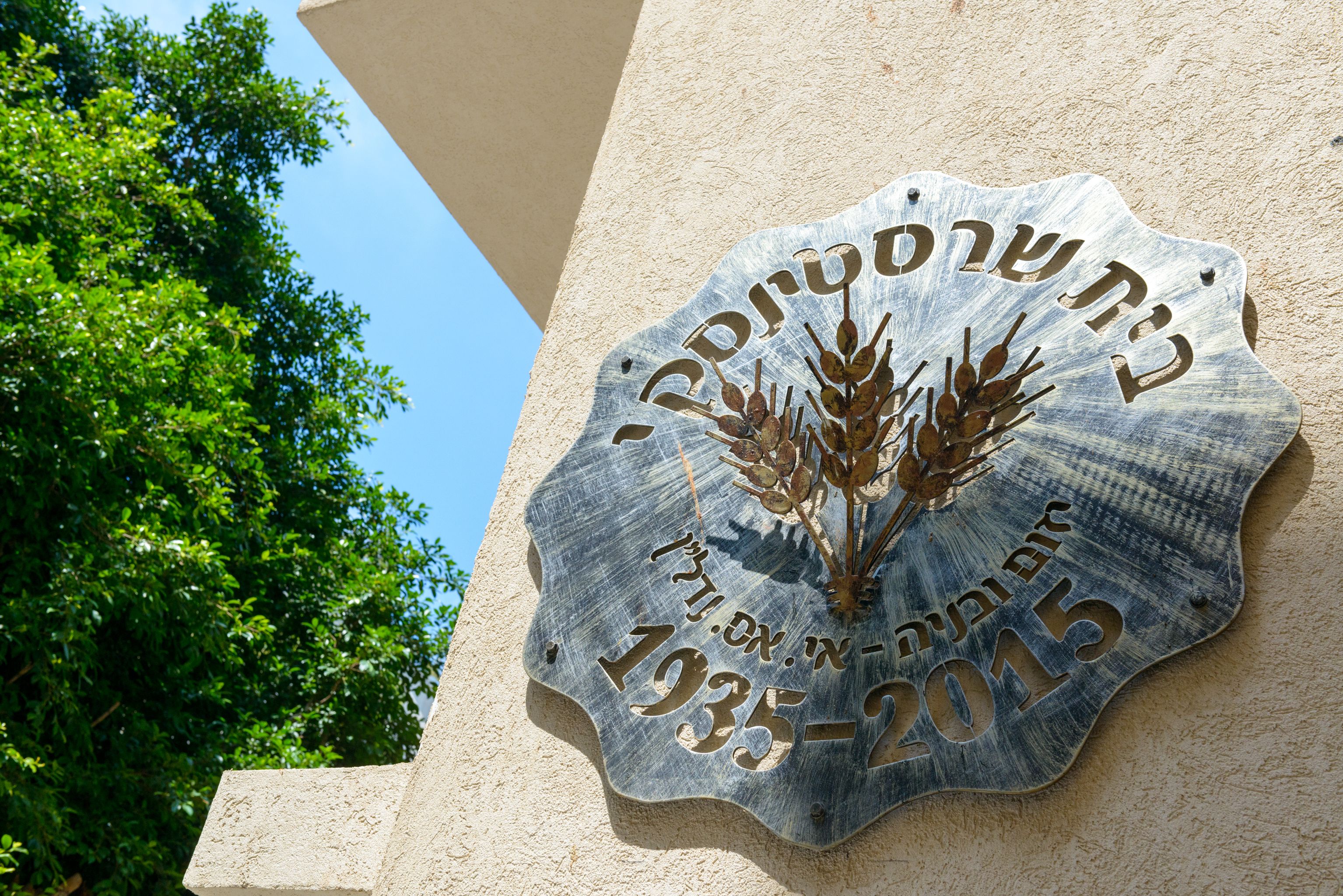 A commemorative plaque with Hebrew text and the years 1935-2015, mounted on a building wall.