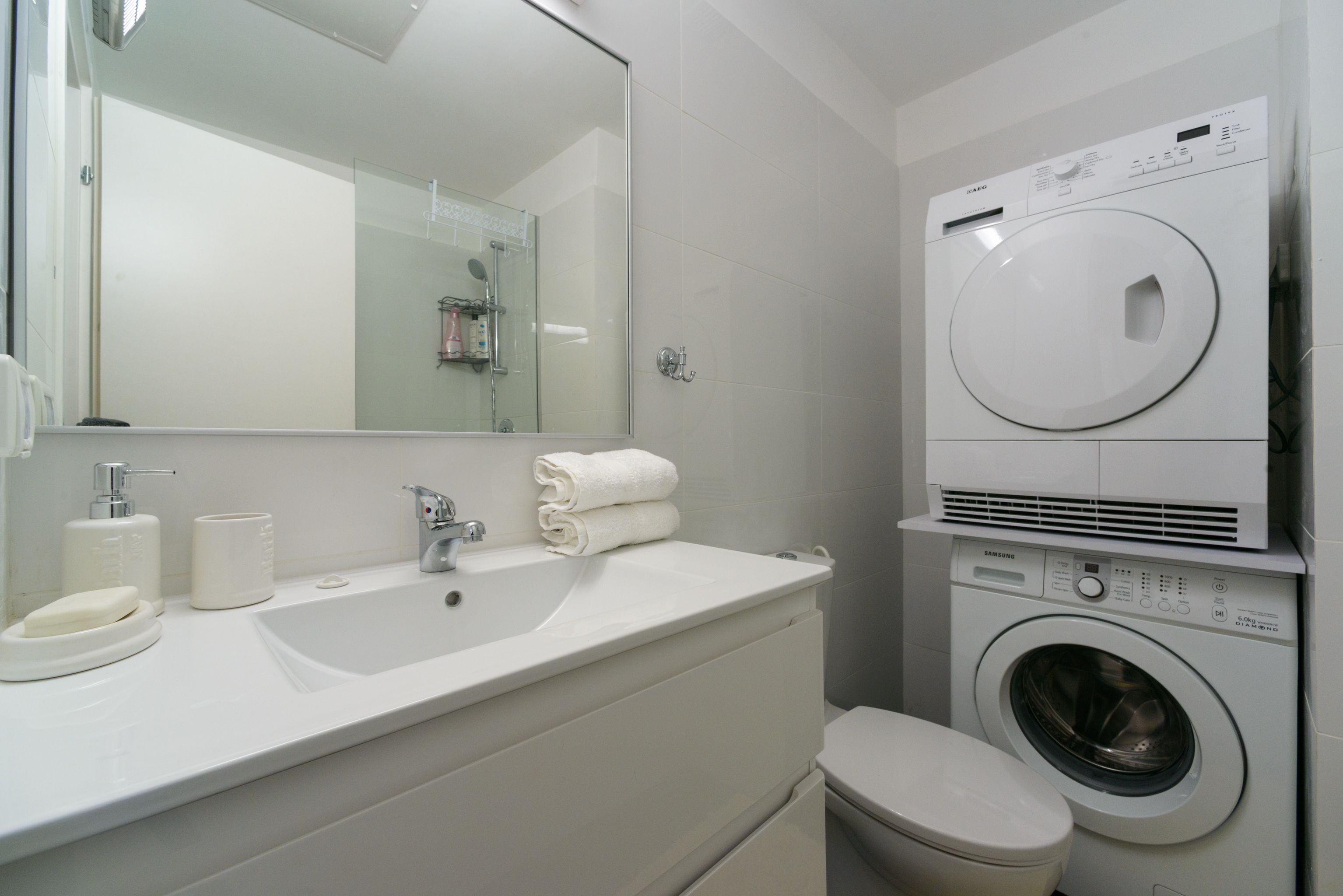A modern bathroom with a white sink, mirror, and stacked washer and dryer.