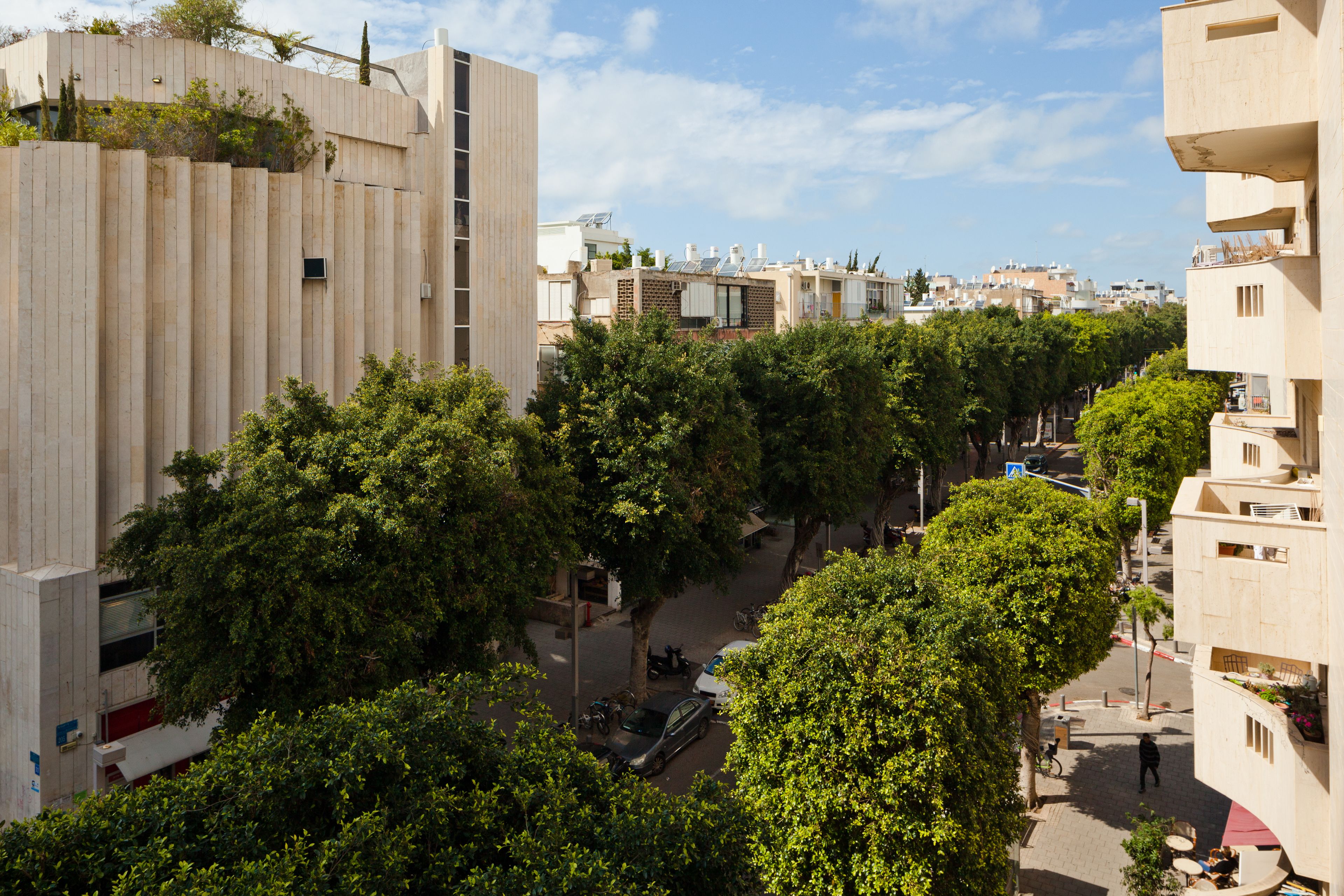 A street view with buildings, trees, and parked cars.