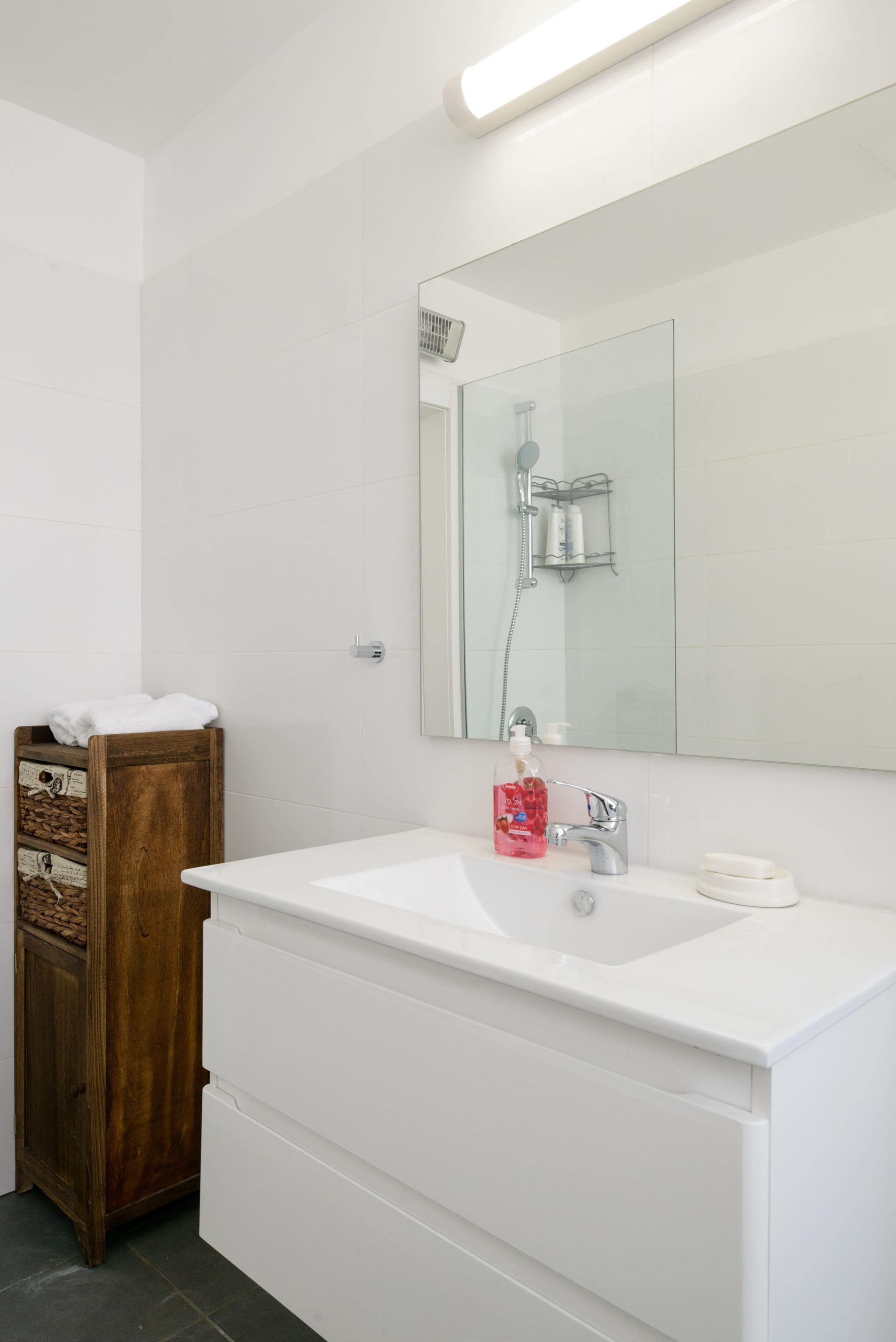 A bathroom with a white sink, a mirror, a wooden cabinet, and a shower area.