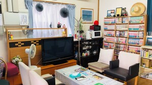 A living room with a television, sofa, chairs, a table with papers, a bookshelf, and a clock on the wall.