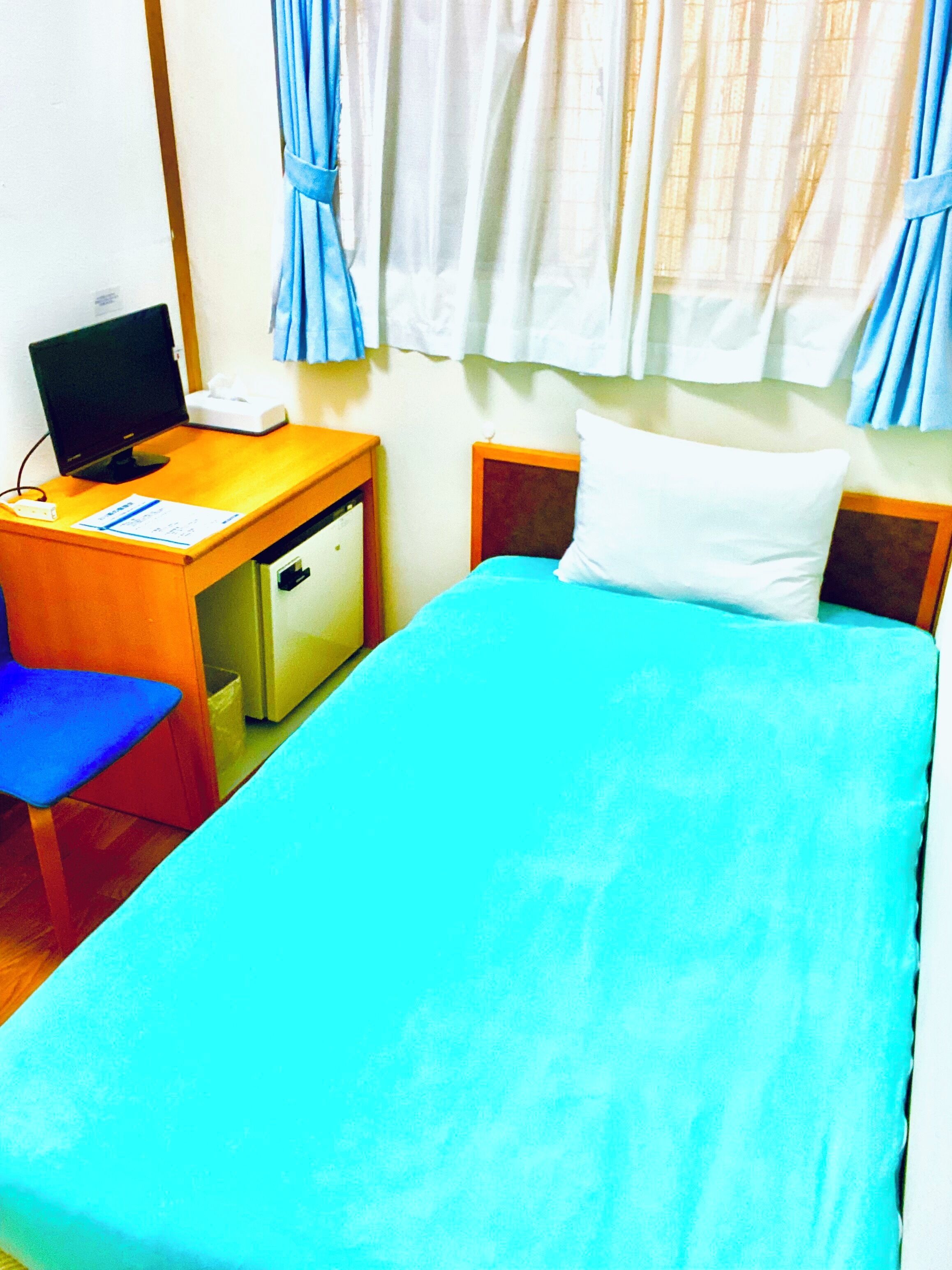 Une chambre comprenant un lit, un bureau avec un ordinateur, une chaise et un petit réfrigérateur.
