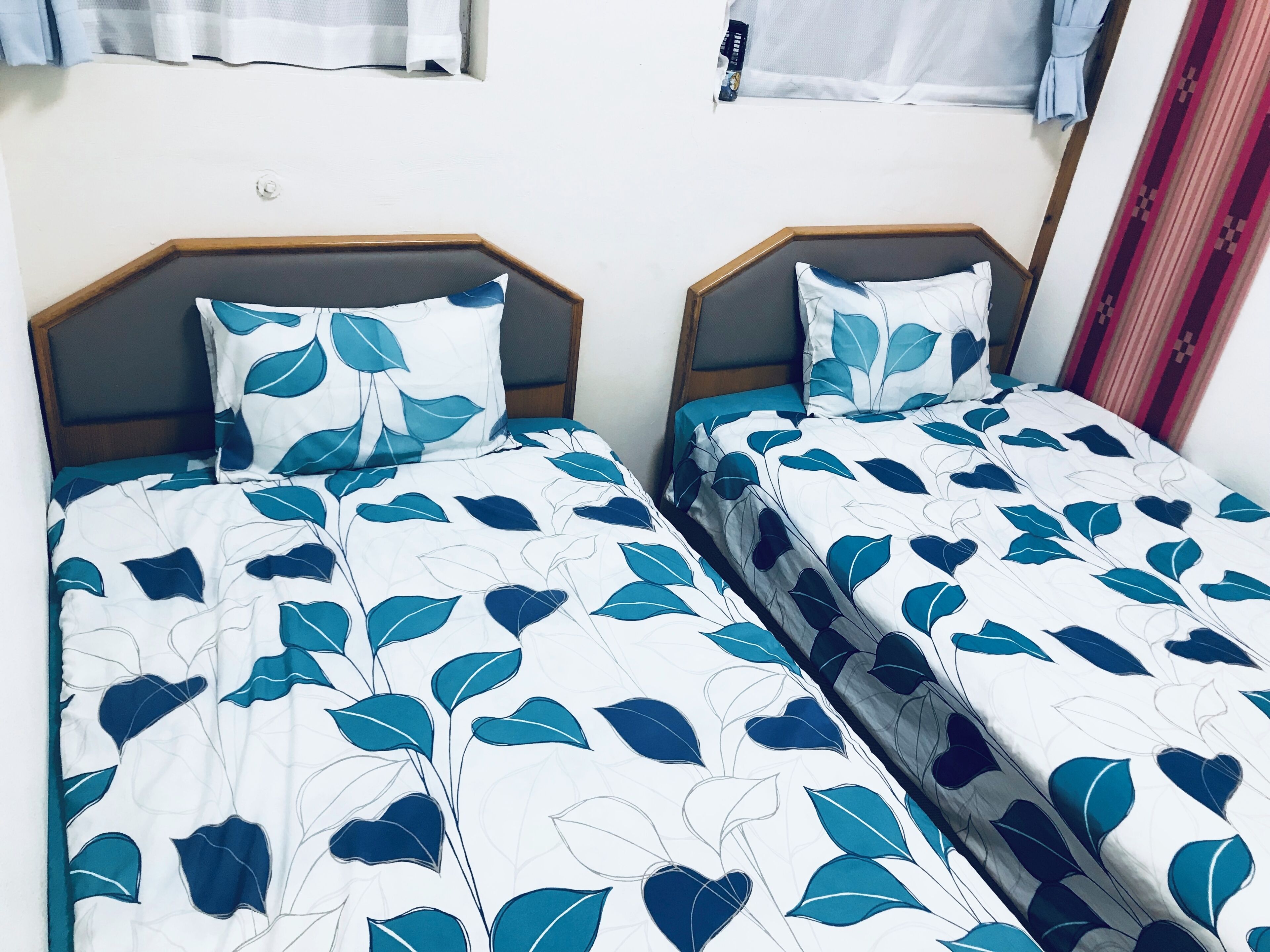 Deux lits jumeaux avec une literie à motifs de feuilles, des têtes de lit en bois et un mur sobre.