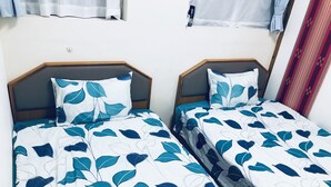 Two twin beds with leaf-patterned bedding, wooden headboards, and a plain wall.