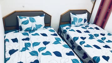 Duas camas de solteiro com roupa de cama estampada em folhas, cabeceiras de madeira e uma parede lisa.