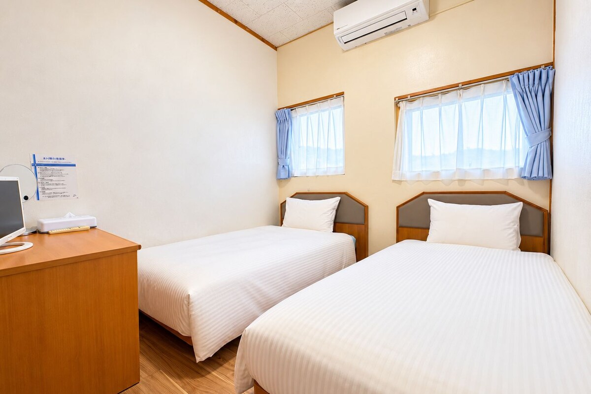 A hotel room with two beds, a desk with a computer, and an air conditioning unit.