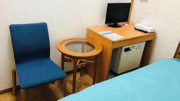 Quarto com uma cama, escrivaninha com computador, cadeira e uma pequena geladeira.