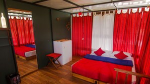 A room with a wooden floor, a bed with red and blue bedding, a small wooden table, and a mirror on the wall. - Whispering Willows (Ootacamund)