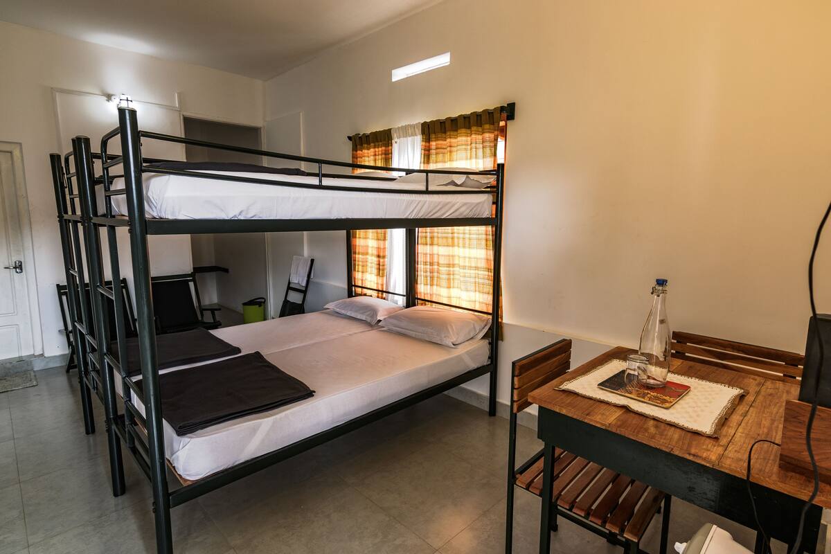Habitación con literas, una mesa y sillas, un escritorio y una ventana con cortinas.