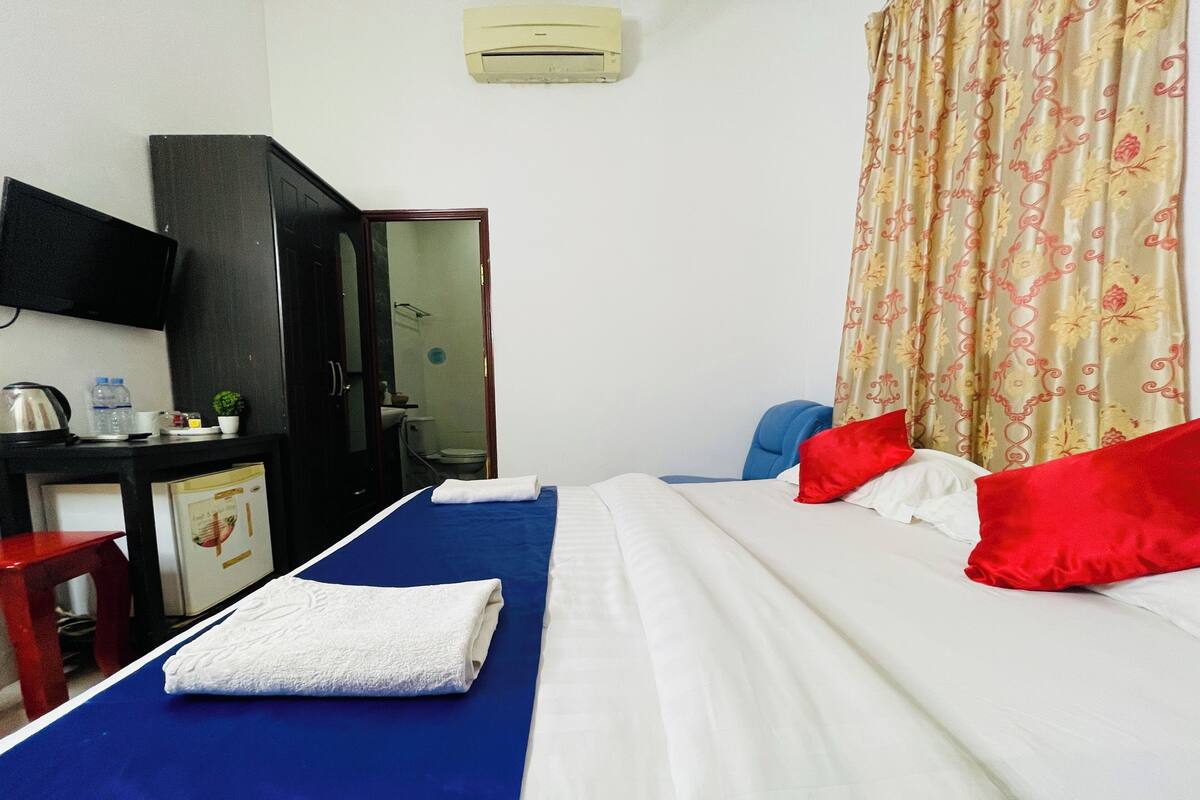Habitación de hotel con cama, escritorio con silla, armario y baño visible a través de una puerta abierta.