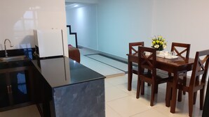 A compact kitchen with a black countertop, a white refrigerator, and a dining area with a wooden table and chairs. - New Season Riverside Hotel (Phnom Penh)