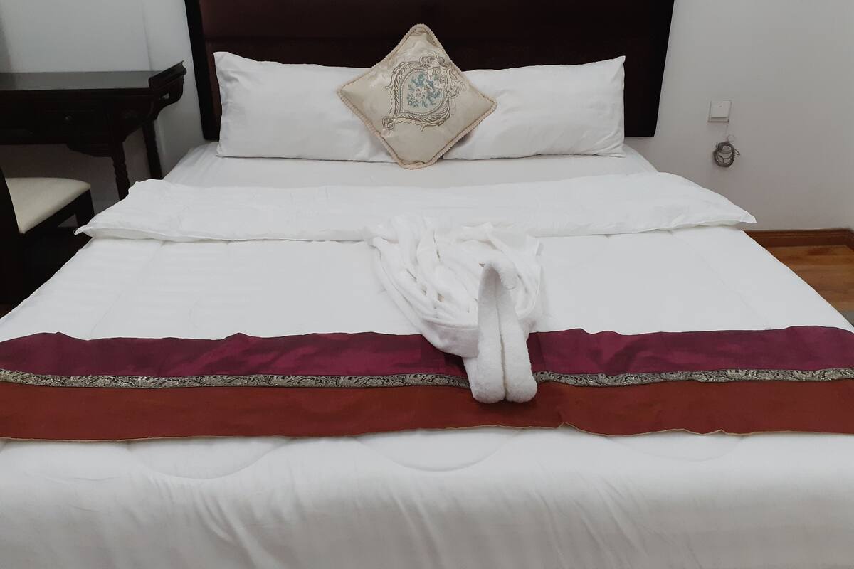 Una cama bien hecha con sábanas blancas, una almohada decorativa y una toalla sobre la cama.