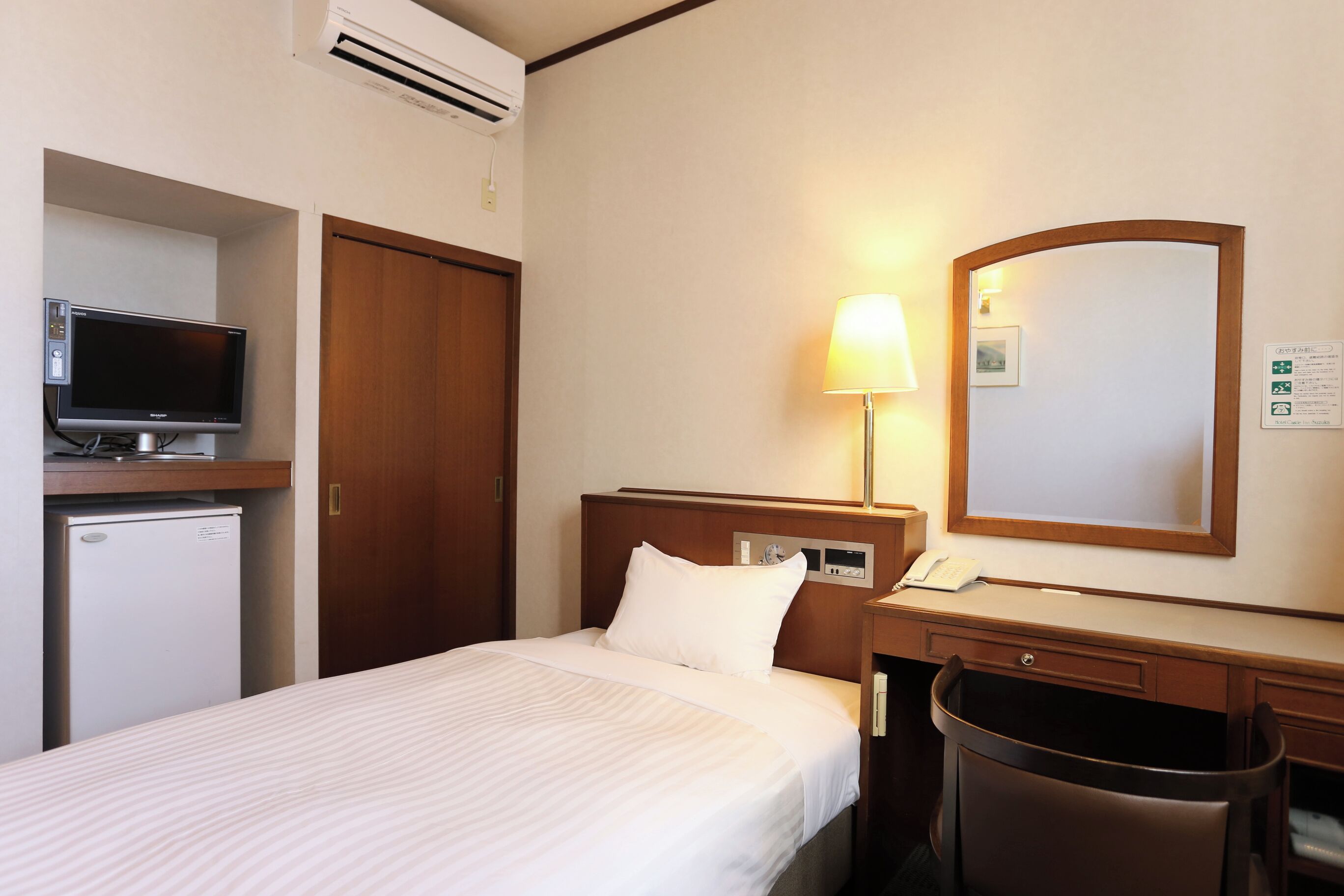 Een hotelkamer met een bed, een bureau, een stoel, een televisie, een lamp en een afvalbak.