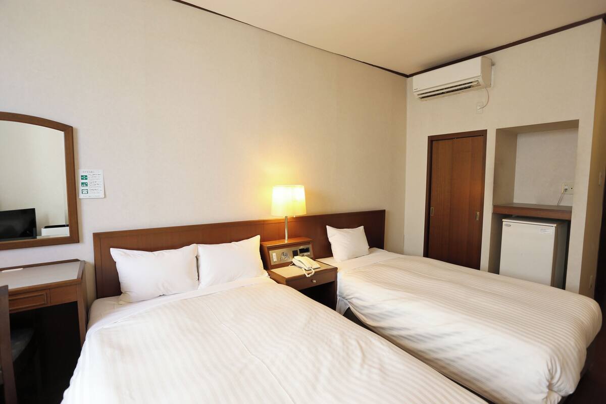 A hotel room with two beds, a desk, a lamp, a phone, and a mini-fridge.