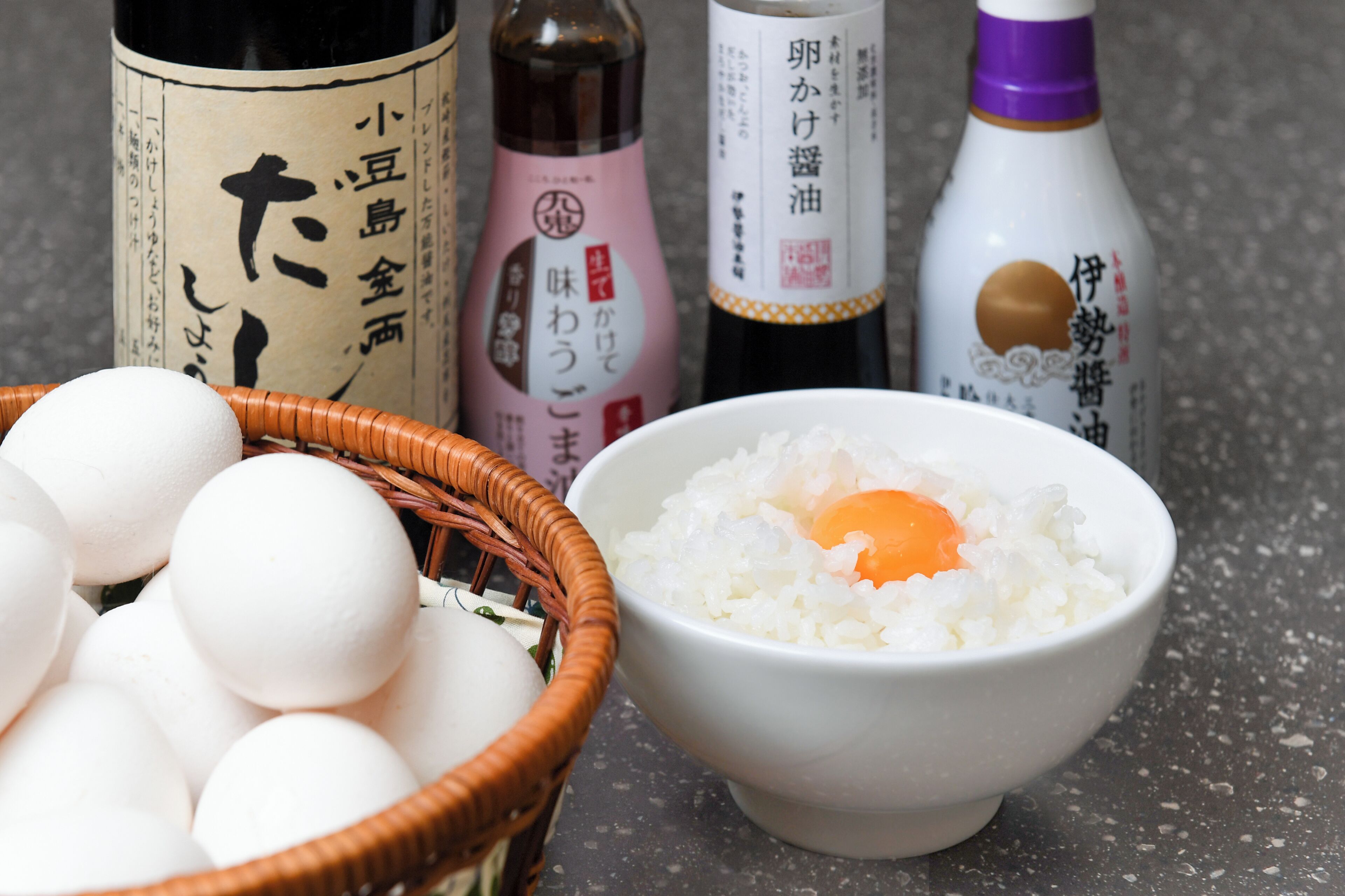 A bowl of rice with an egg, a basket of eggs, and bottles of soy sauce and other condiments.