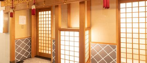 A traditional Japanese room with tatami flooring, shoji screens, and a wooden ceiling.