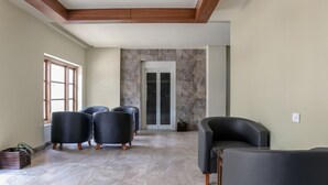 A spacious living area with a high ceiling, a stone wall, and a sliding glass door leading to a balcony. - Treebo Casino (Kozhikode)