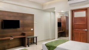 A hotel room with a flat-screen TV mounted on a wooden wall, a small table, a bed with a green bedspread, and a wooden door. - Treebo Casino (Kozhikode)