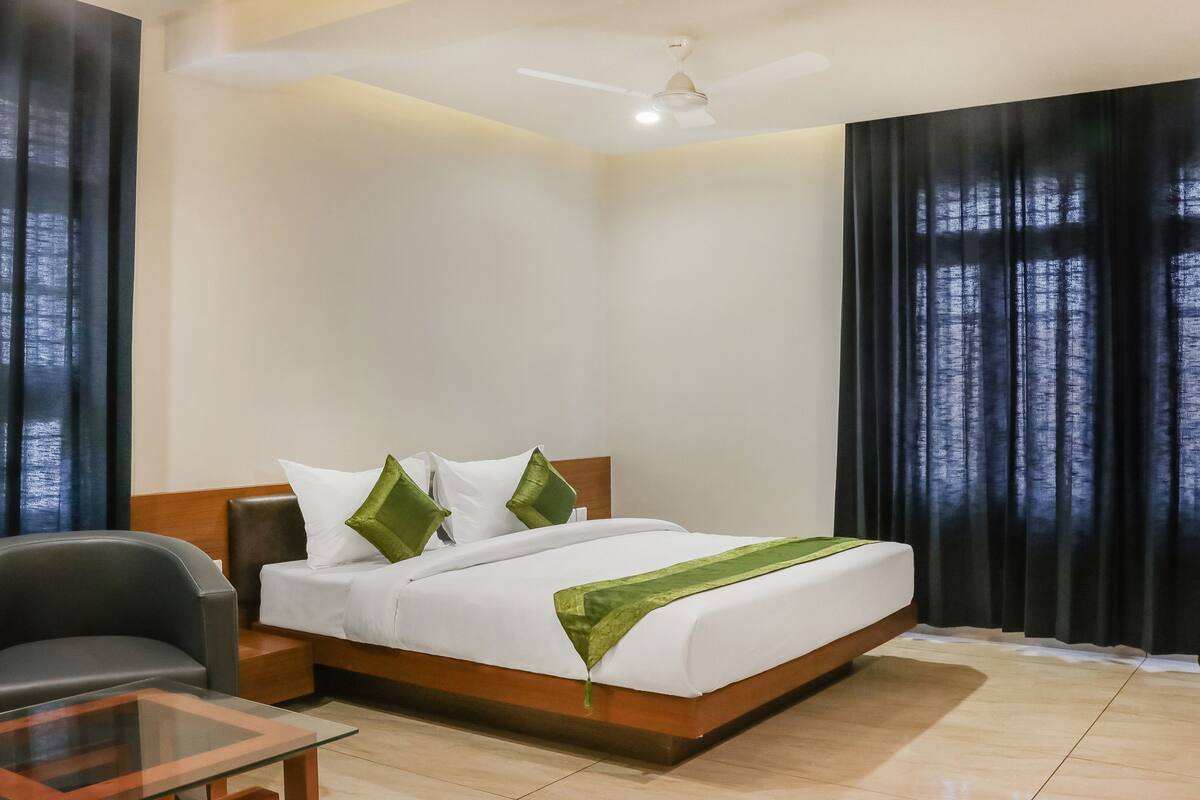 Una habitación de hotel con cama, una silla, una mesita de vidrio y un ventilador de techo.
