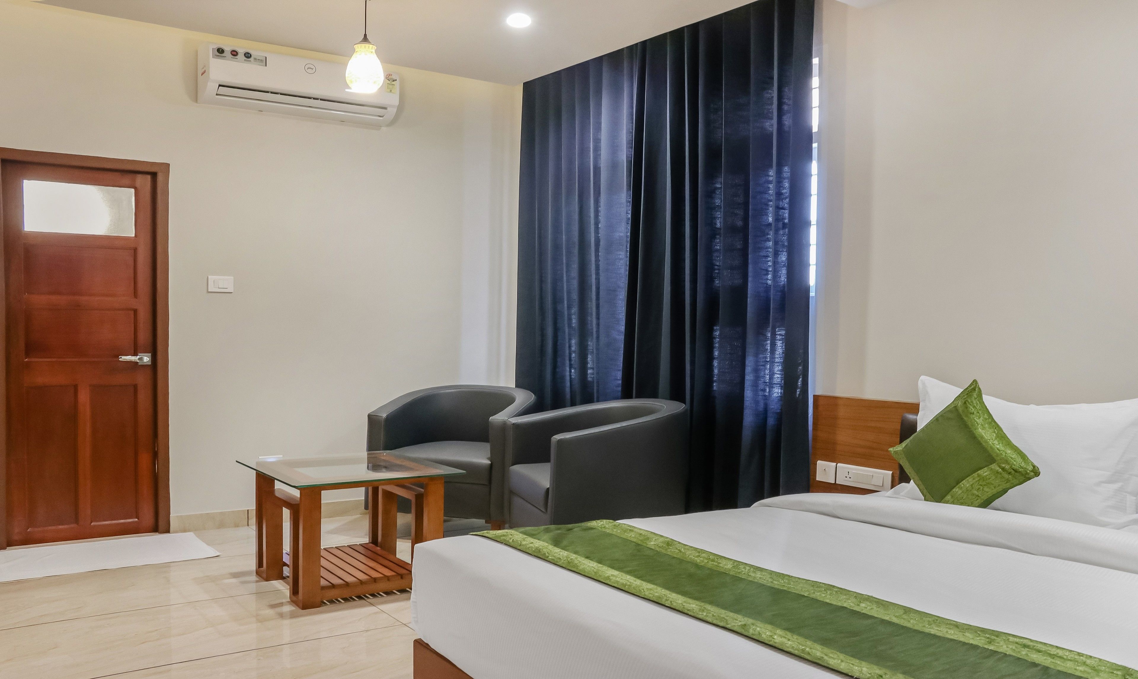 A hotel room with a bed, a desk, a chair, a window with curtains, and an air conditioning unit.