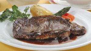 Un steak à la croûte bien dorée, servi avec une pomme de terre bouillie et quelques légumes verts sur une assiette blanche.
