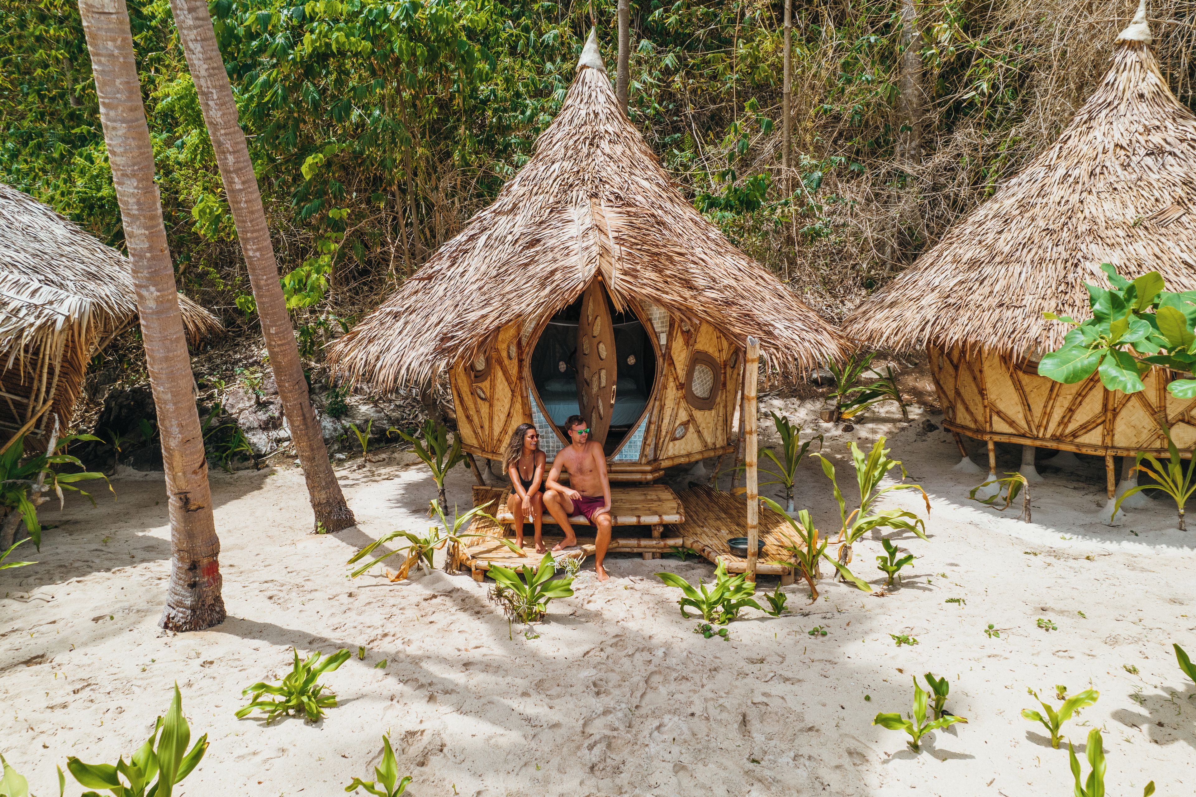 A beach setting with thatched-roof huts and palm trees.