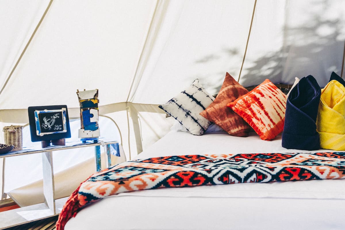 Un lit avec une couverture à motifs, plusieurs oreillers, une petite table sur laquelle est posé un cadre photo, et une structure en forme de tente en arrière-plan.
