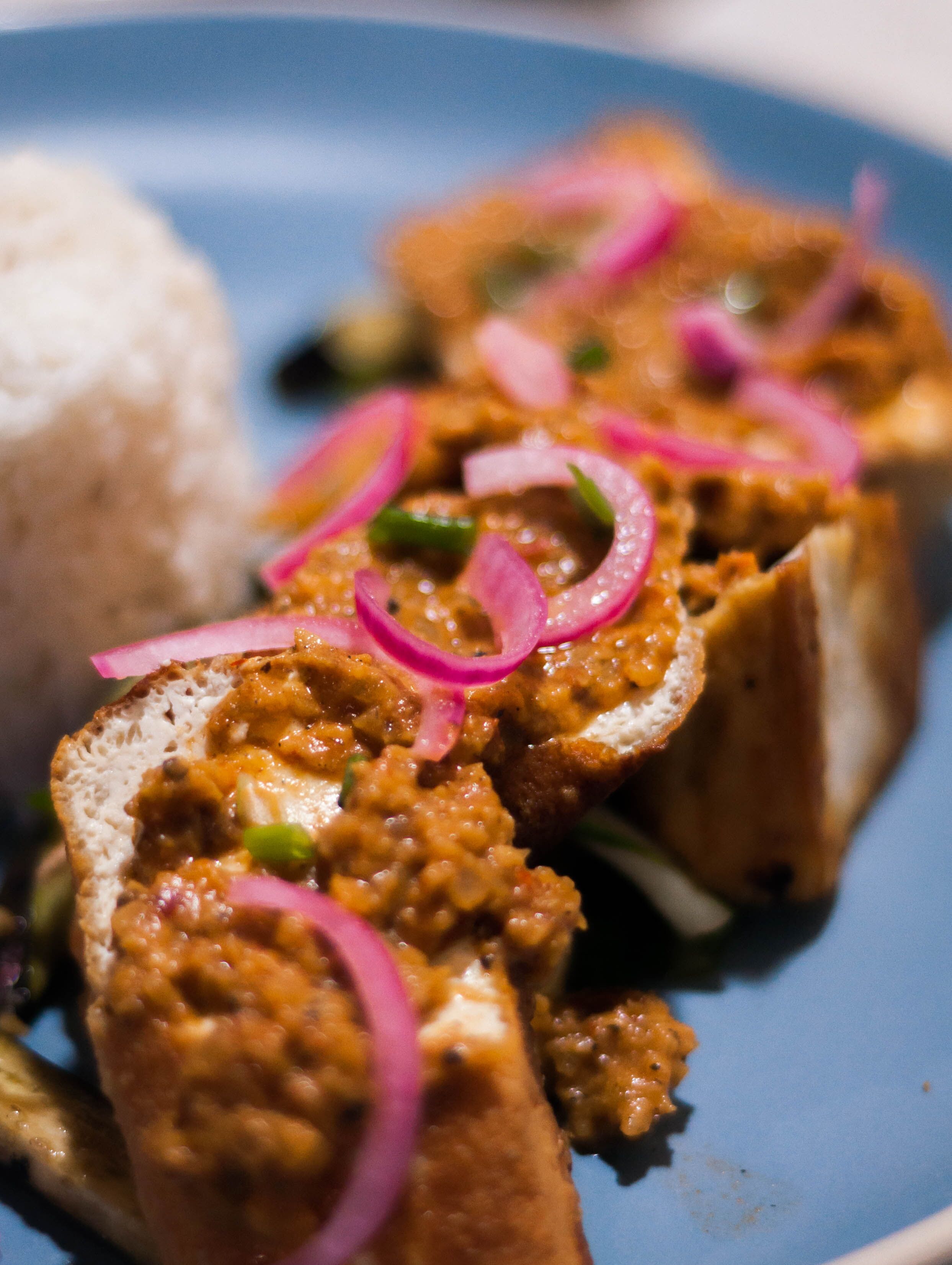 A plate with sliced meat topped with red onion rings, accompanied by a side of white rice.