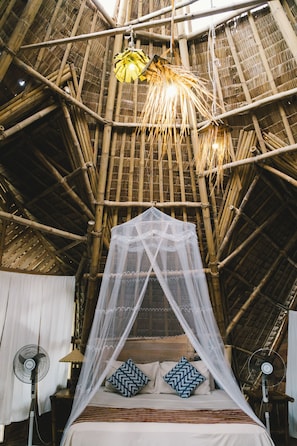 A room with a bed under a bamboo ceiling, a mosquito net, and two fans. - DRYFT Darocotan Island (El Nido)