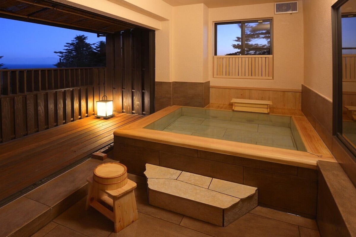 Un onsen japonais traditionnel, doté d’une terrasse en bois, d’un bain à eau chaude et d’une lanterne.
