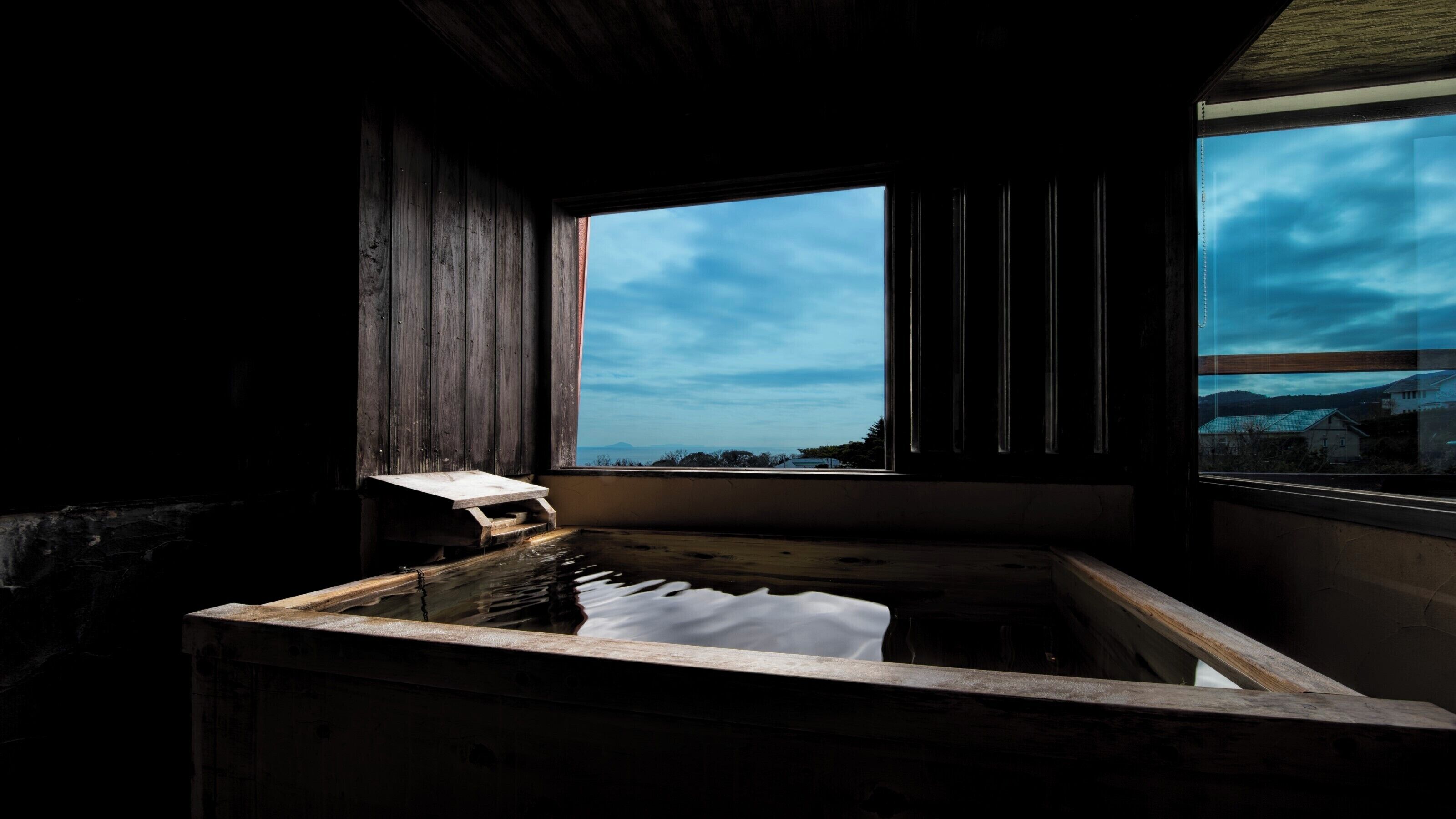 Ein rustikaler Holzraum mit einem großen Fenster, einer Holzbank und Blick auf eine weite Landschaft.
