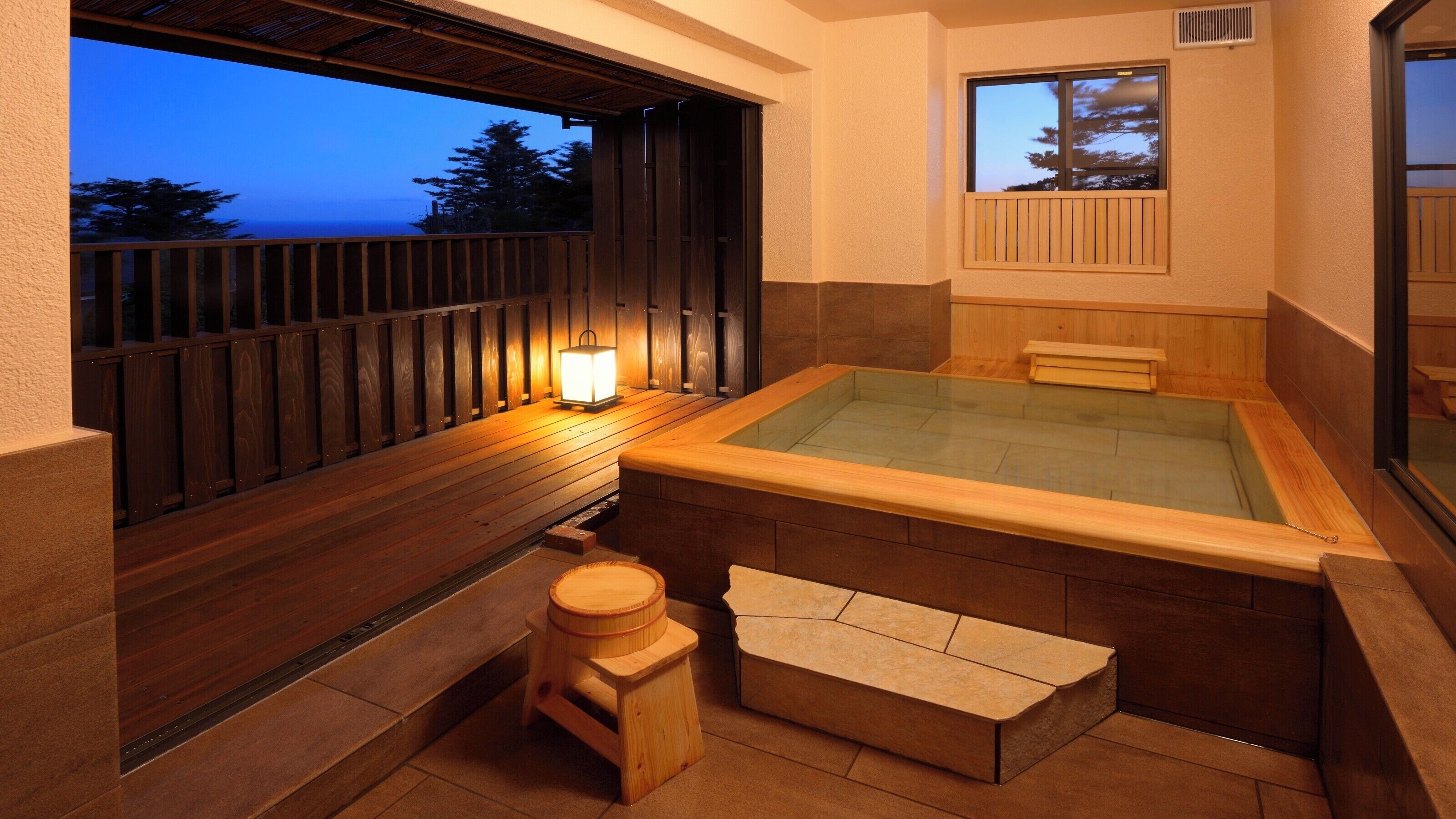 Ein Whirlpool mit einer Holzterrasse, einem kleinen Hocker und einem Fenster mit Blick auf ein Gewässer.