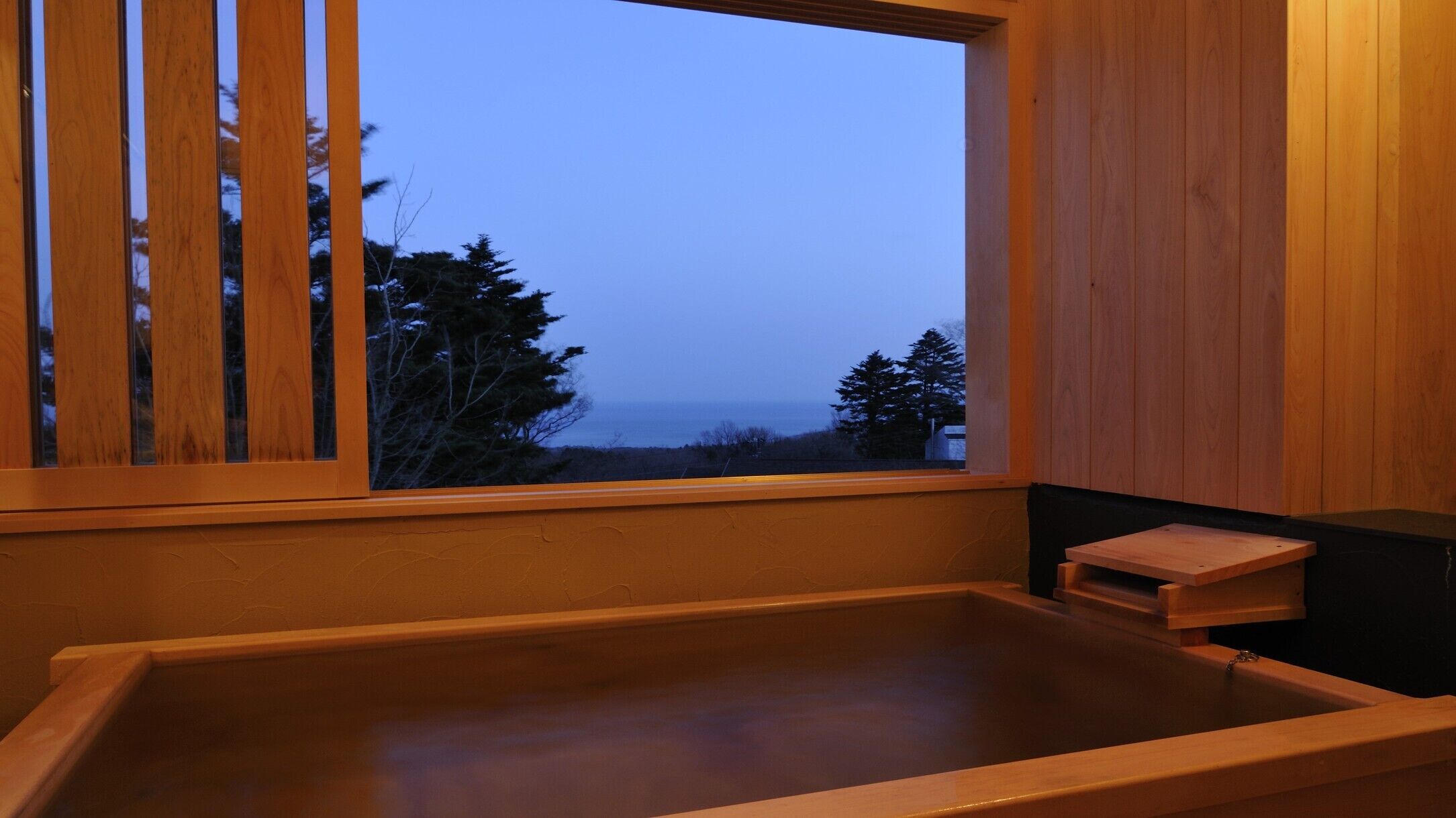 Eine hölzerne Badewanne mit Blick auf Bäume und das Meer.