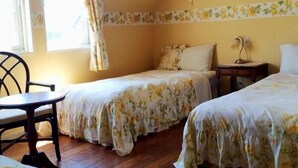 A bedroom with two beds, a wooden floor, a small table, and a window with curtains. - Country House Hotel Avonlea (Ito)