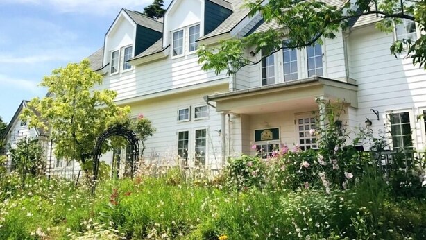 A two-story house with a porch and a garden in front. - Country House Hotel Avonlea (Ito)