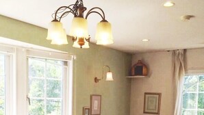A dining area with a wooden table and chairs, a chandelier, and large windows with curtains. - Country House Hotel Avonlea (Ito)