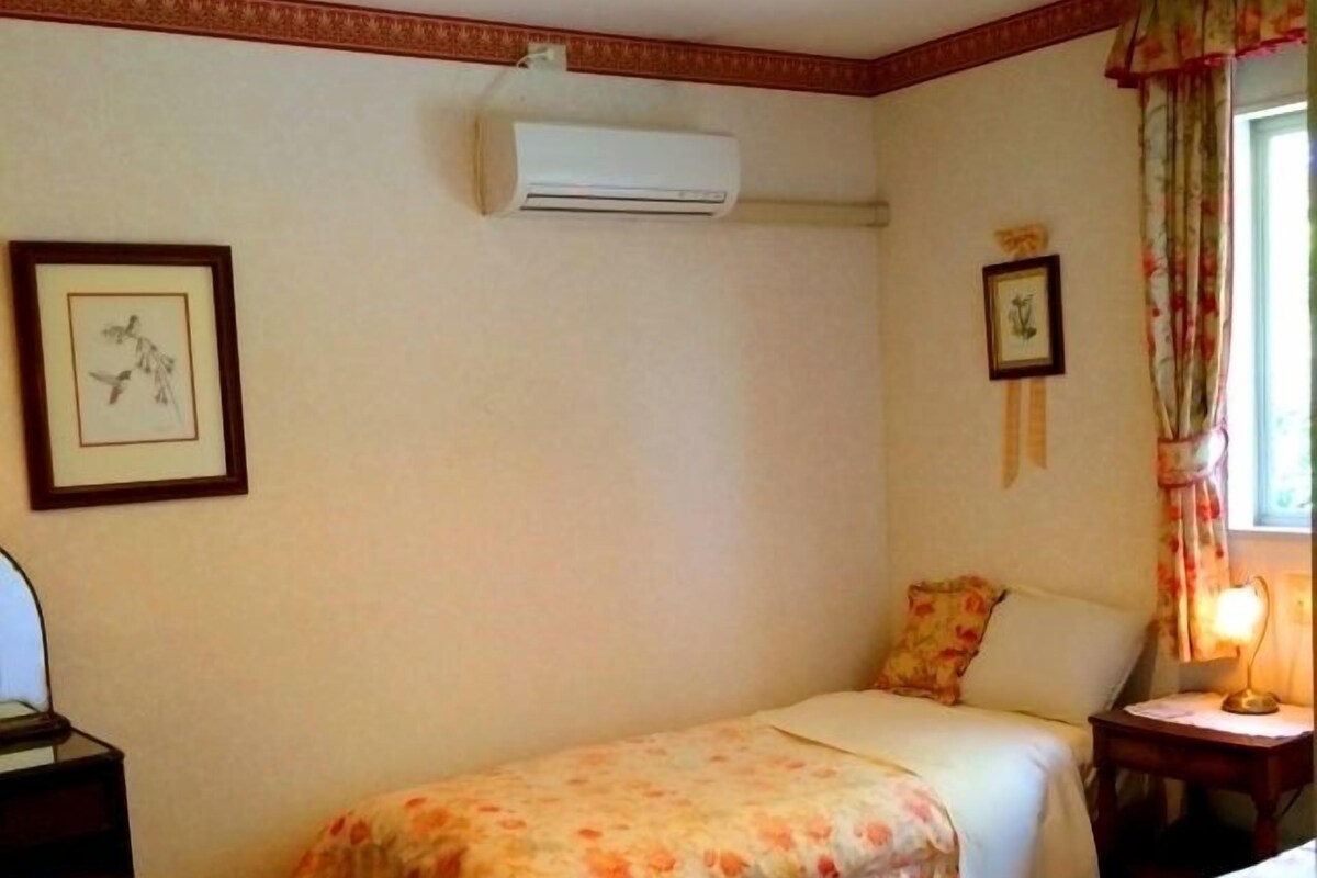 A small, cozy room with a single bed, a bedside table, a nightstand, and a window with curtains.