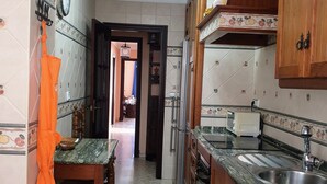Une cuisine avec un mur recouvert de carreaux, des meubles en bois, un évier et un coin repas avec des chaises.