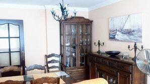 Un salon comprenant un canapé, un meuble en bois, une table à manger avec des chaises, un lustre et un ventilateur.