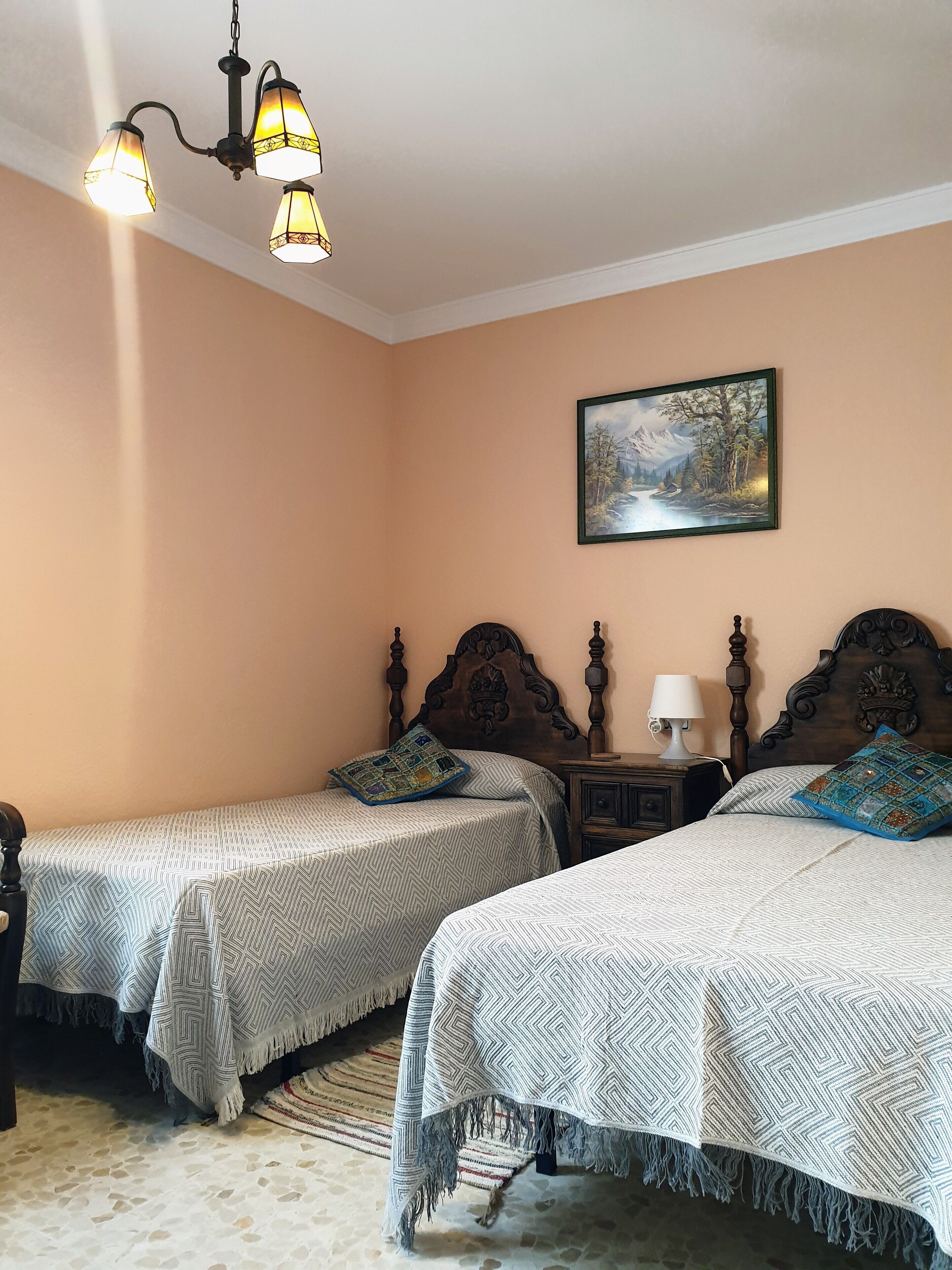 Une chambre avec deux lits, un tableau au mur et un lustre.