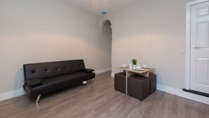A modern room with a black sofa, a small table with cups and a plant, and a white door. - Townhouse @ Rose Street Stoke (Stoke-on-Trent)