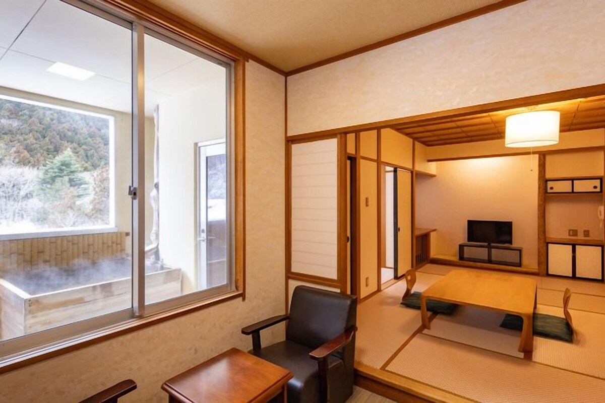 A traditional Japanese room with tatami flooring, a low table, a chair, a television, and sliding doors.