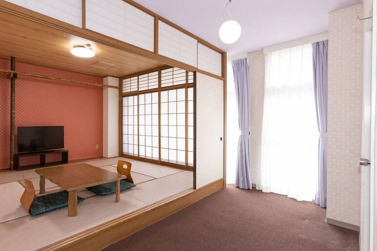 A traditional Japanese room with tatami flooring, a television, a low table, and sliding doors.