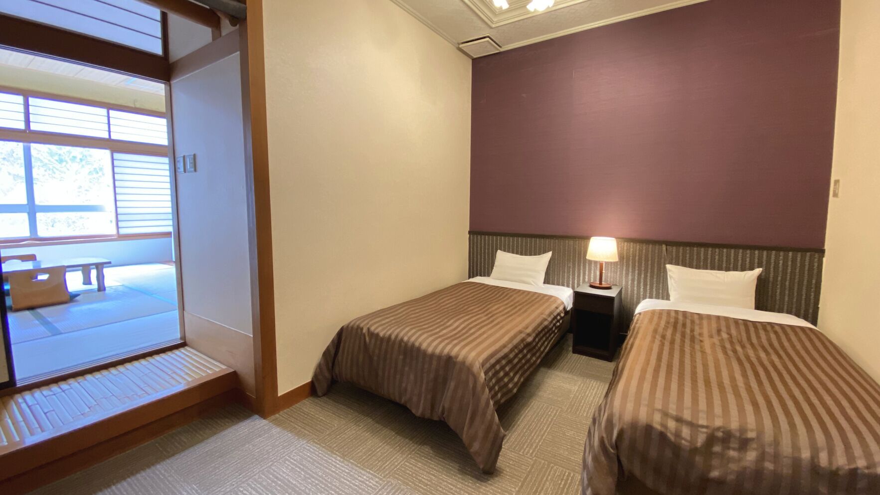 Een hotelkamer met twee bedden, een nachtkastje met een lamp, een schuifdeur naar een balkon en uitzicht op de omgeving.