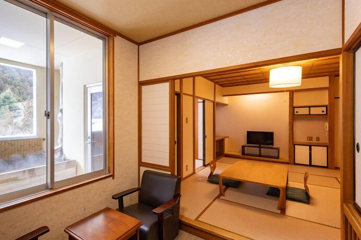 A traditional Japanese room with tatami flooring, a low table, a chair, a television, and sliding doors.