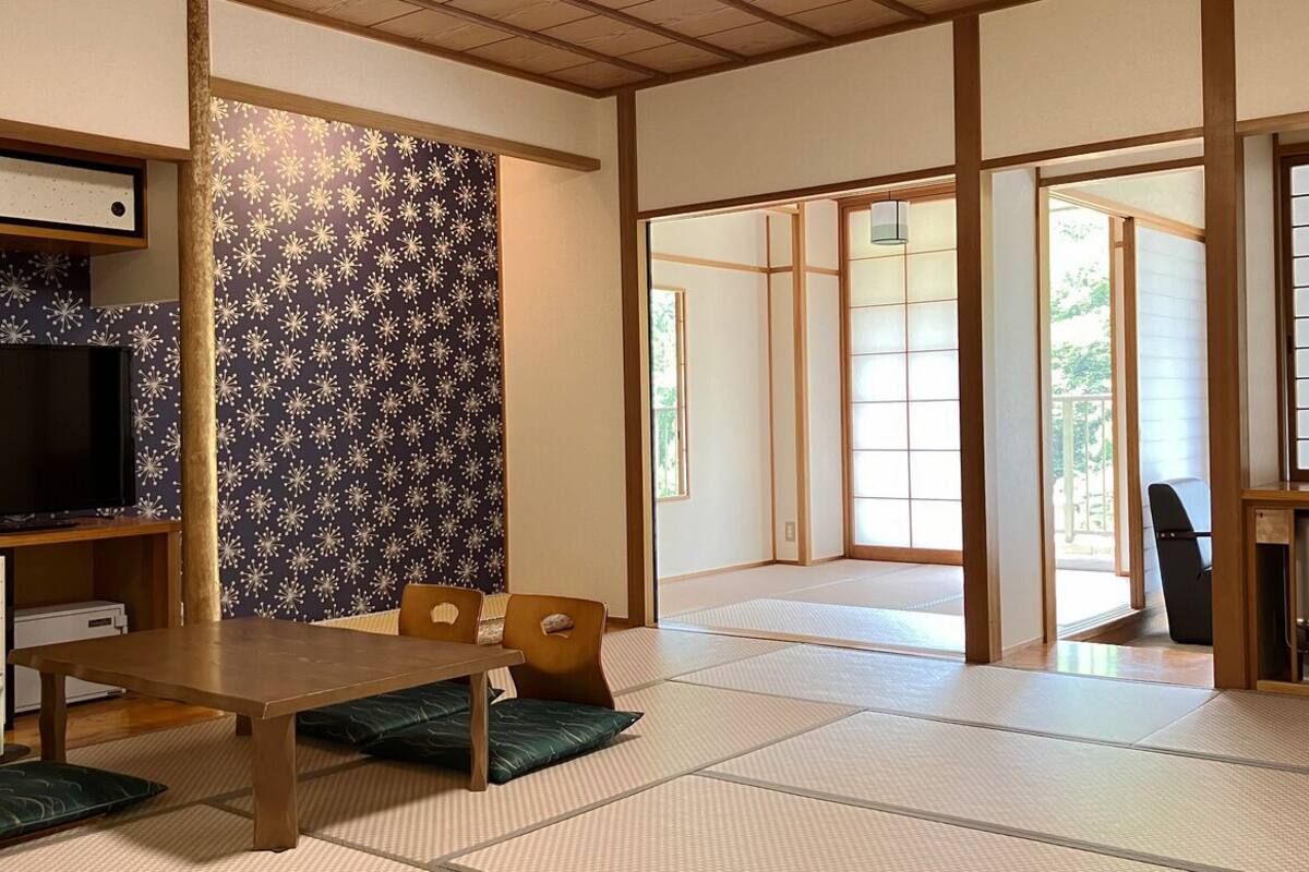 A traditional Japanese room with tatami flooring, a low table, and sliding doors leading to an outdoor area.
