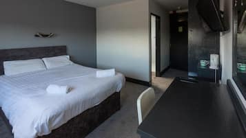 Una habitación de hotel con cama, escritorio, televisor y puerta que da a un baño.