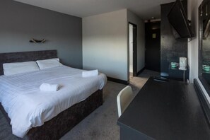 Ein Hotelzimmer mit einem Bett, einem Schreibtisch, einem Fernseher und einer Tür zu einem Badezimmer.