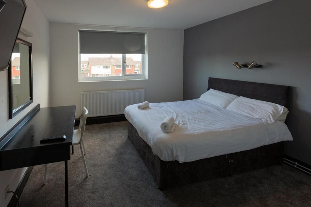 A bedroom with a bed, a desk, a chair, a window, and a radiator.